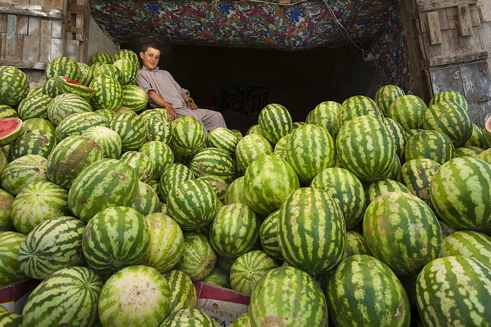 A boy in a market rests on a giant pile of water melons, Herat, Afghanistan, Asia