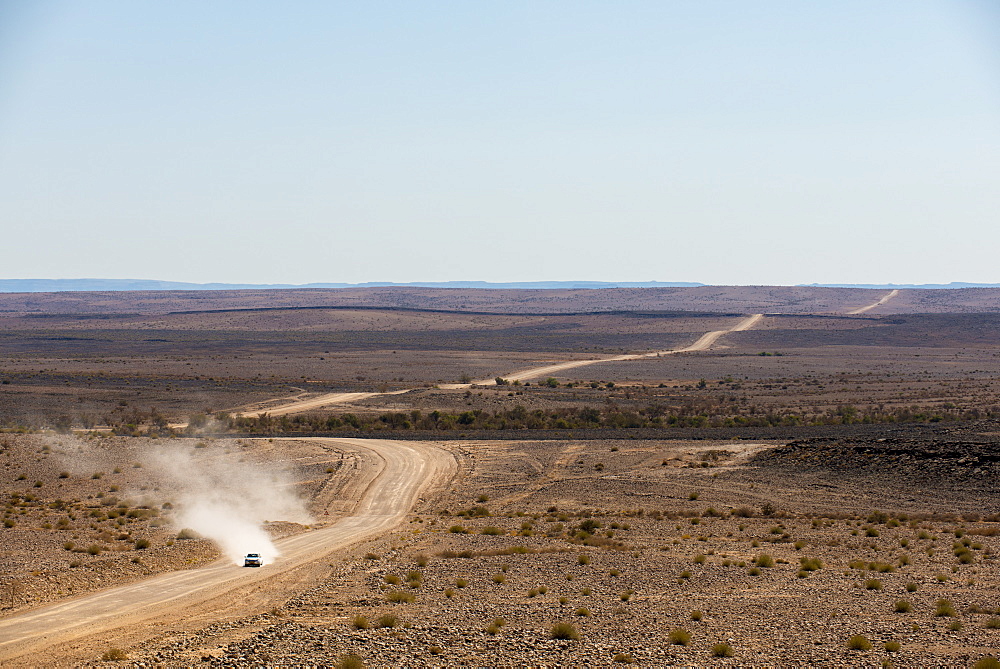 A car leaves a cloud of dust as it apporachs along the long dusty road from the Fish River Canyon, Namibia, Africa