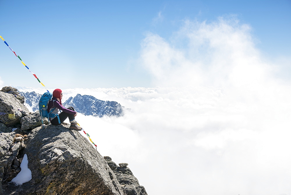 A woman sits under prayer flags marking the top of the Laurebina La, the pass between the Langtang region and Helmabu, Himalayas, Nepal, Asia