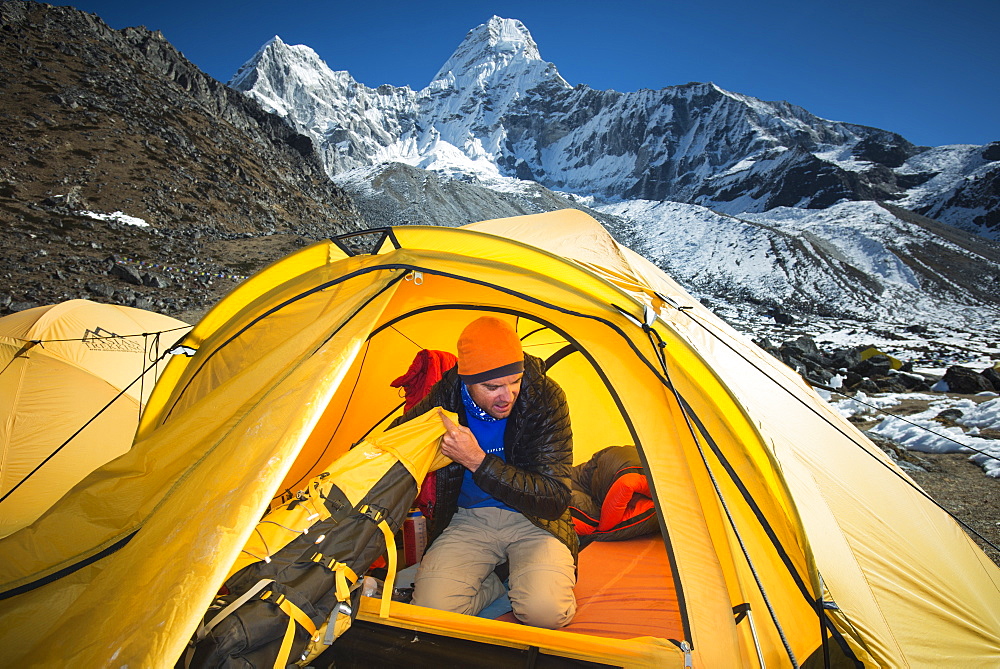 A mountaineer packs his bag in preparation to climb Ama Dablam, the 6856m peak in the distance, Khumbu Region, Himalayas, Nepal, Asia