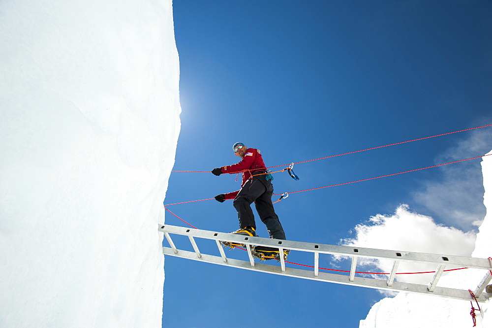 A climber on Everest makes his way across a crevasse using a temporary ladder, Khumbu Region, Nepal, Asia