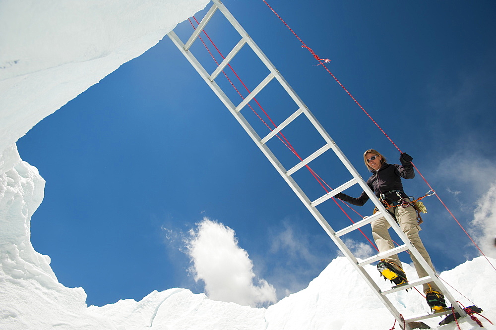 A climber on Everest makes her way across a crevasse using a temporary ladder, Khumbu Region, Himalayas, Nepal, Asia