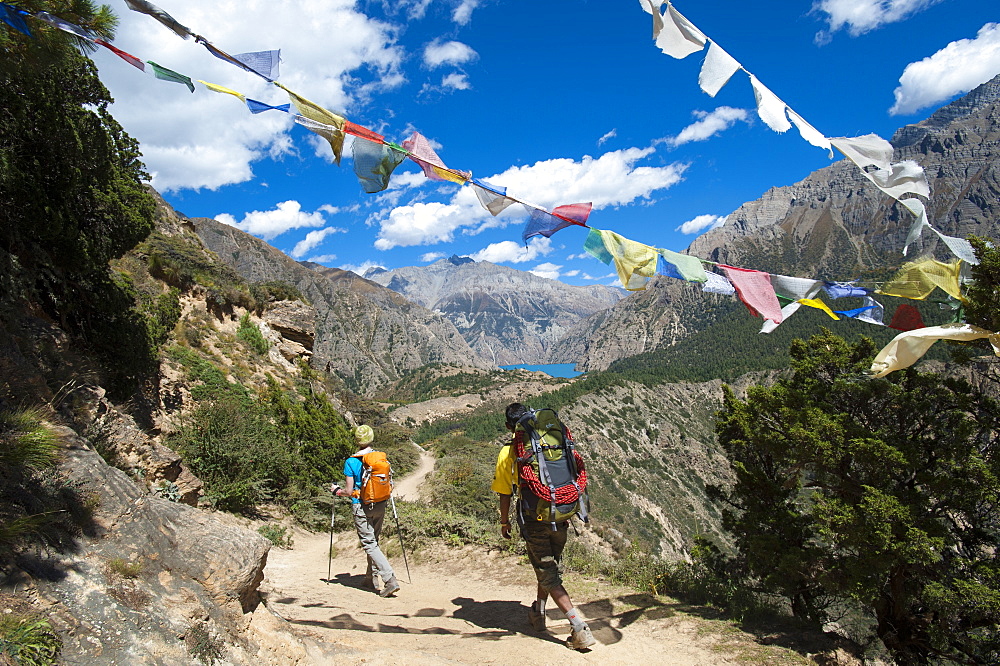 Prayer flags mark a high point in the trail where trekkers are rewarded with their first glimpse of Phoksundo Lake, Dolpa Region, Himalayas, Nepal, Asia