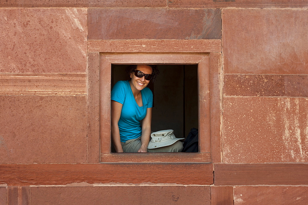 A tourist peeks out from one the windows within the Fatehpur Sikri temple complex, Uttar Pradesh, India, Asia