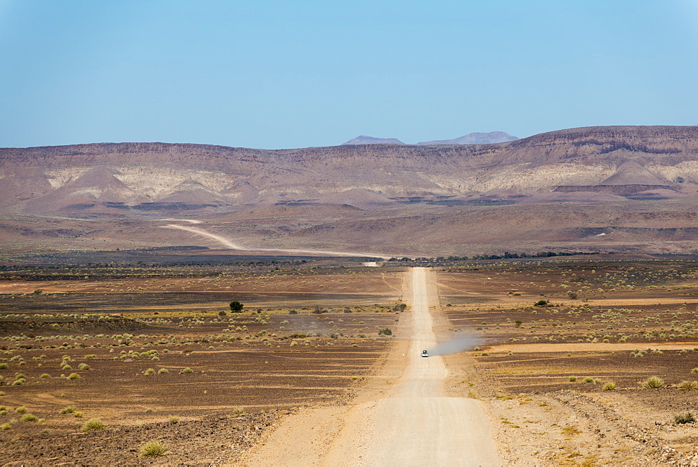 A 4x4 car leaves a cloud of dust as it apporachs along the long dusty road to the Fish River Canyon, Namibia, Africa