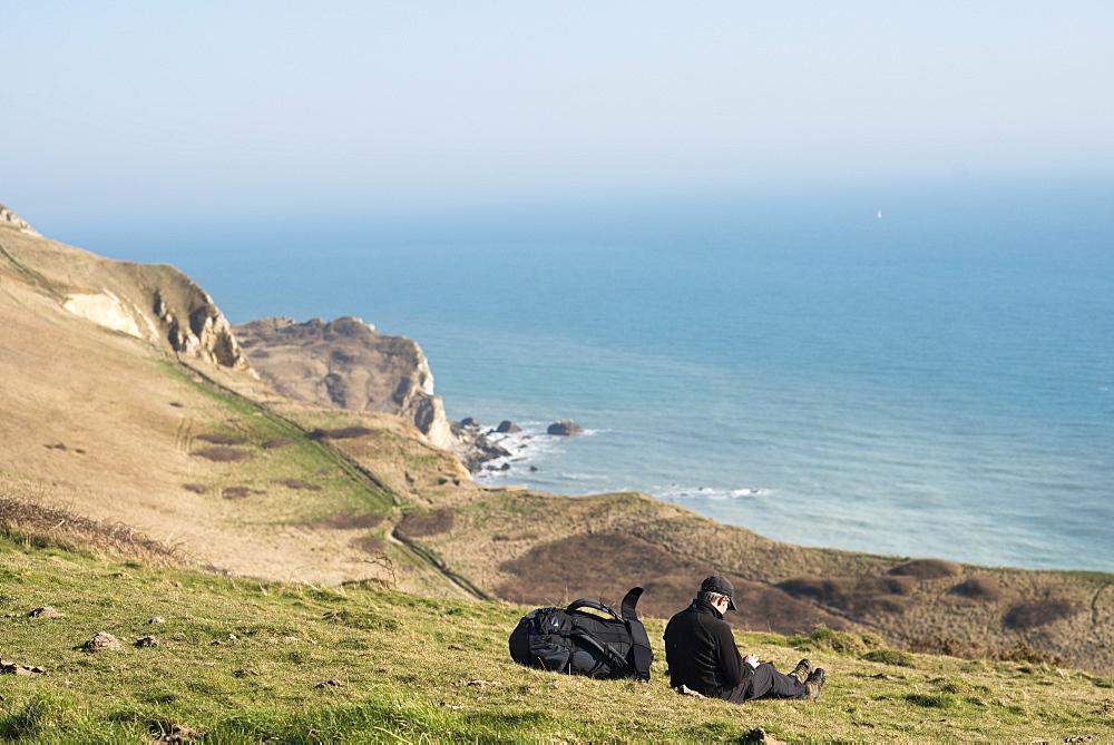 A man takes a break from a coastal walk near Lulworth Cove in Dorset, Jurassic Coast, UNESCO World Heritage Site, England, United Kingdom, Europe