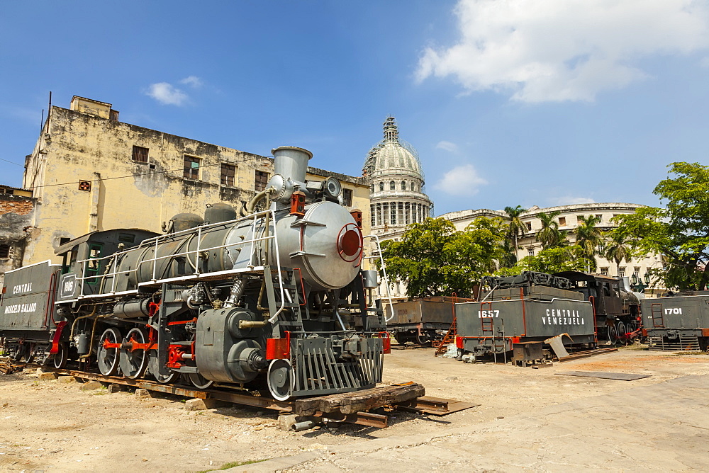 A vintage steam train in a restoration yard with the dome of the former Parliament Building in the background, Havana, Cuba, West Indies, Caribbean, Central America