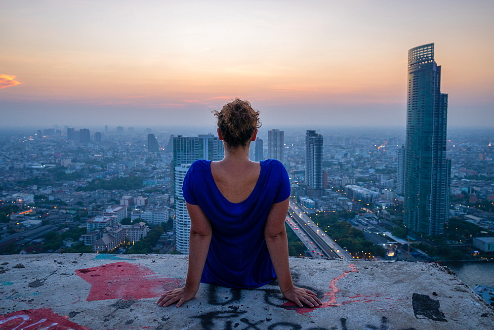 A single woman watching sun set over city skyline at dusk, Bangkok, Thailand, Southeast Asia, Asia