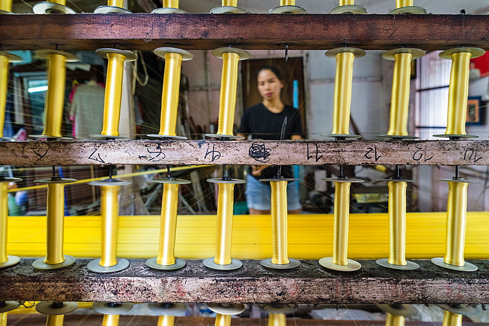 A silk weaver creates a bolt of gold thread at a traditional workshop in Bangkok, Thailand, Southeast Asia, Asia