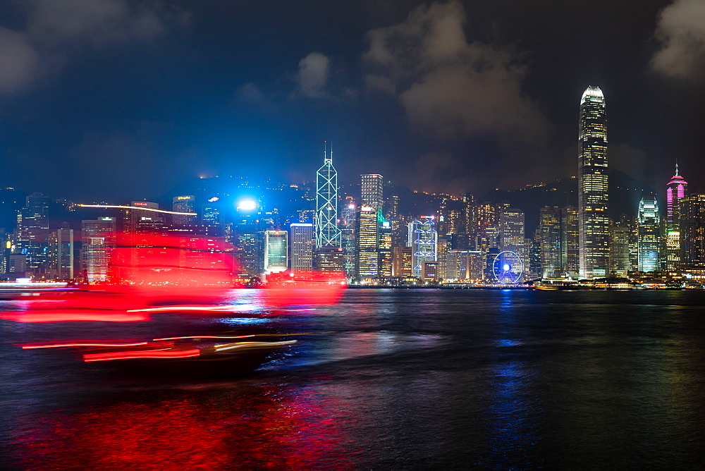 A red junk sailboat glides in front of the Hong Kong skyline at night, Hong Kong, China, Asia