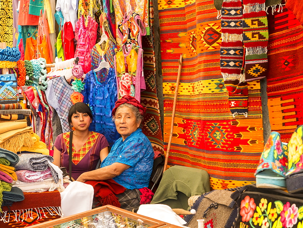 Women talking in market with background of handmade rugs and clothing, Oaxaca, Mexico, North America