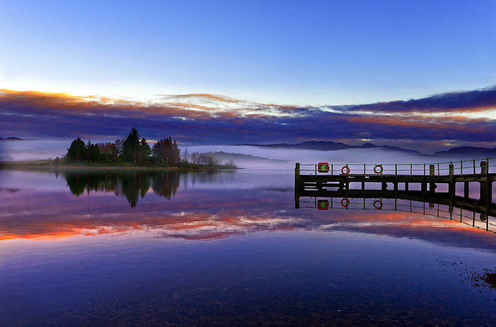 A tranquil view across the calm waters of Loch Shiel as dawn breaks on a misty winter morning. Ardnamurchan, Scottish Highlands, Scotland, United Kingdom, Europe