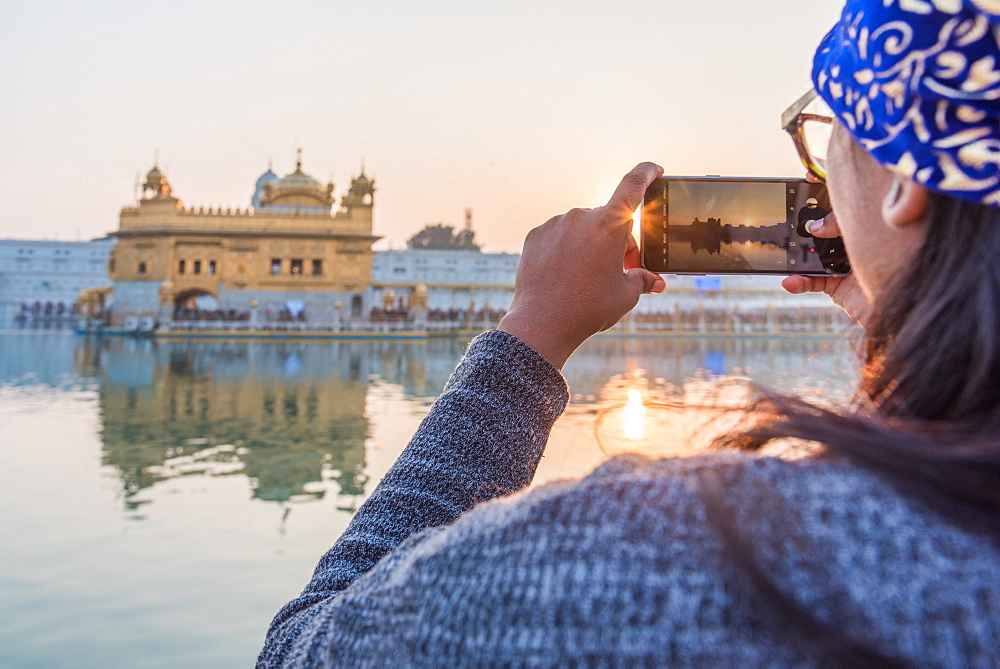 An Indian lady takes a smartphone picture of the Golden Temple at sunset, The Golden Temple, Amritsar, Punjab, India, Asia