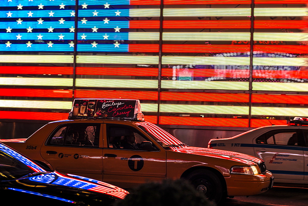 Yellow New York taxi in front of the American flag in Times Square, New York City, United States of America, North America