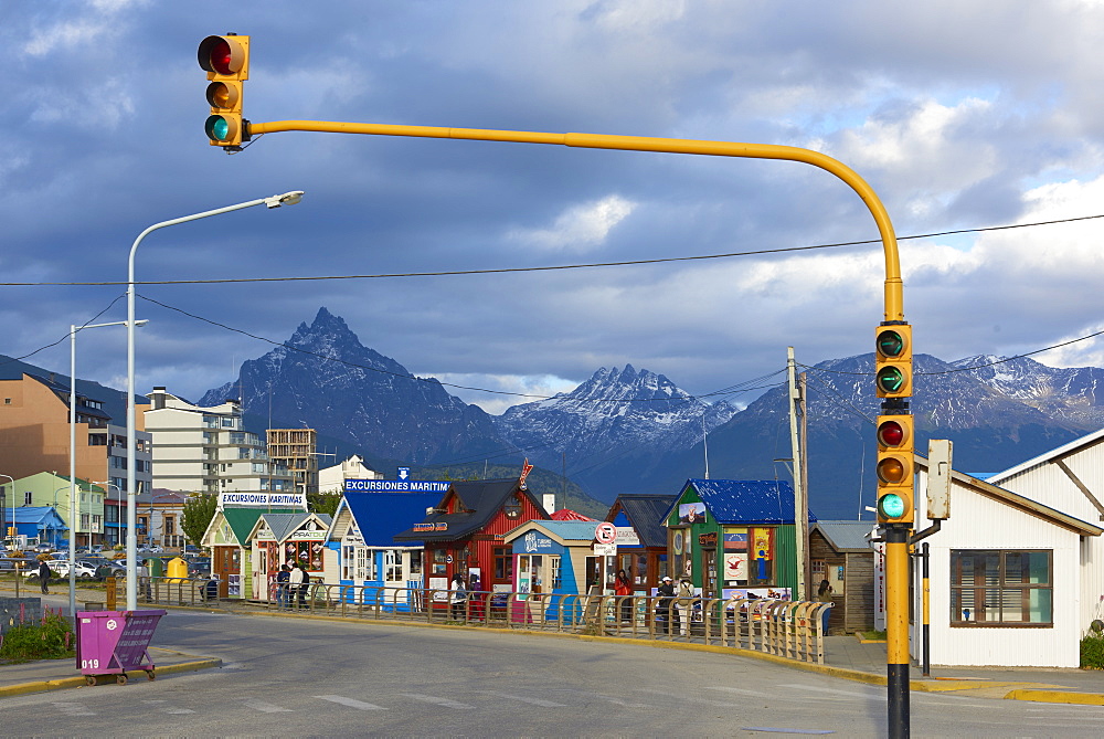 Colourful houses on touristic road framed by traffic lights post with snowy mountain chain beyond, Ushuaia, Argentina, South America