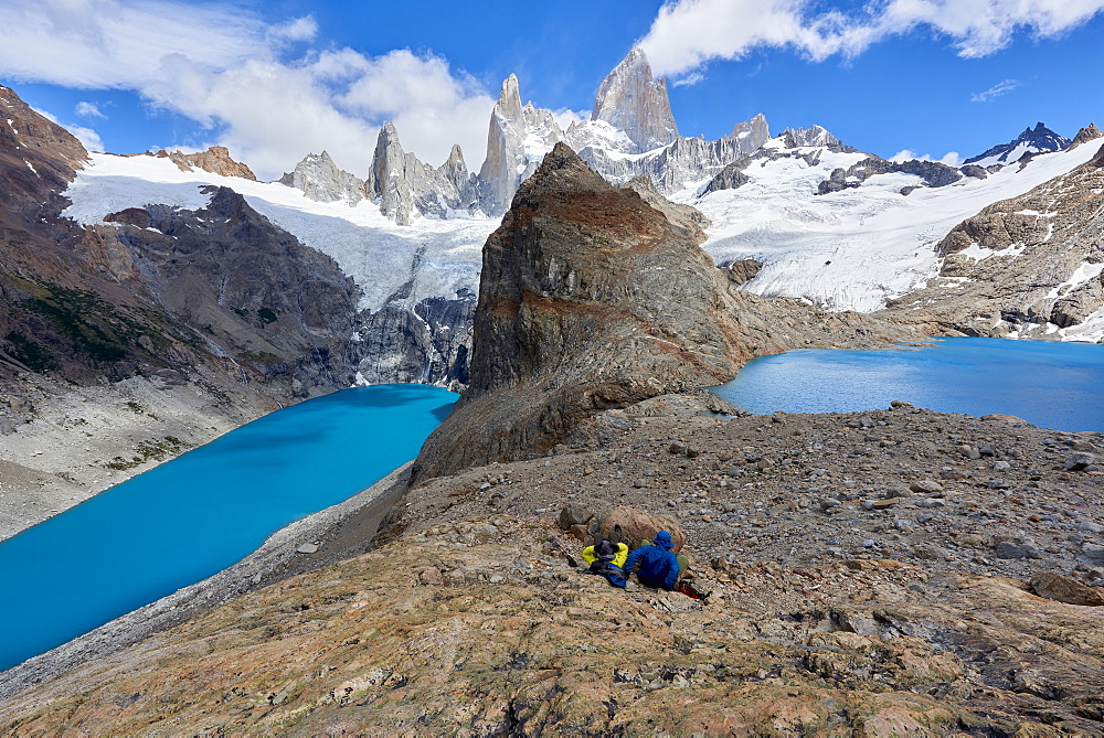 A couple in mountain gear rests on rocks with view to Lago de los Tres and Mount Fitz Roy, Patagonia, Argentina, South America