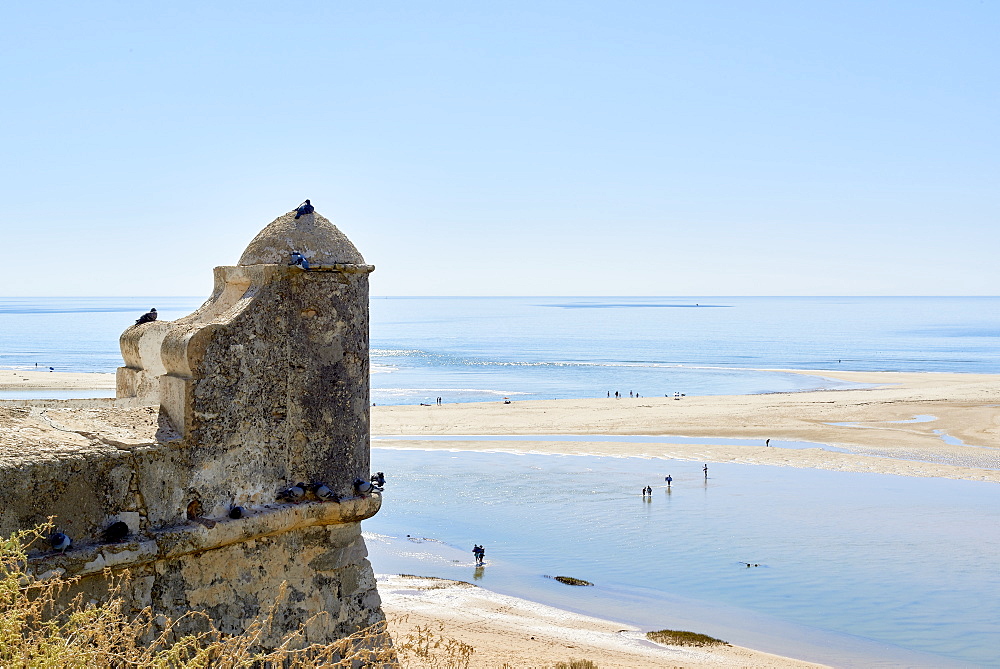 Beachgoers crossing a lagoon formed by the low tide, and detail of a watchtower in Cacela Velha, Algarve, Portugal, Europe