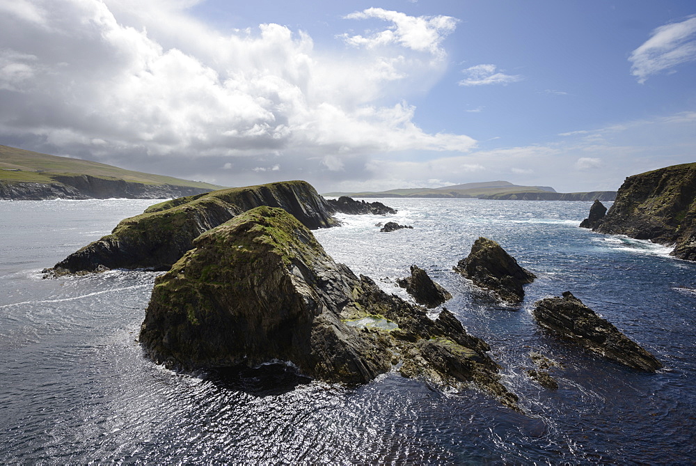 Huge clouds clear the way for bright sunshine to light the cliffs and islands of St. Ninian's Bay, Shetland, Scotland, United Kingdom, Europe