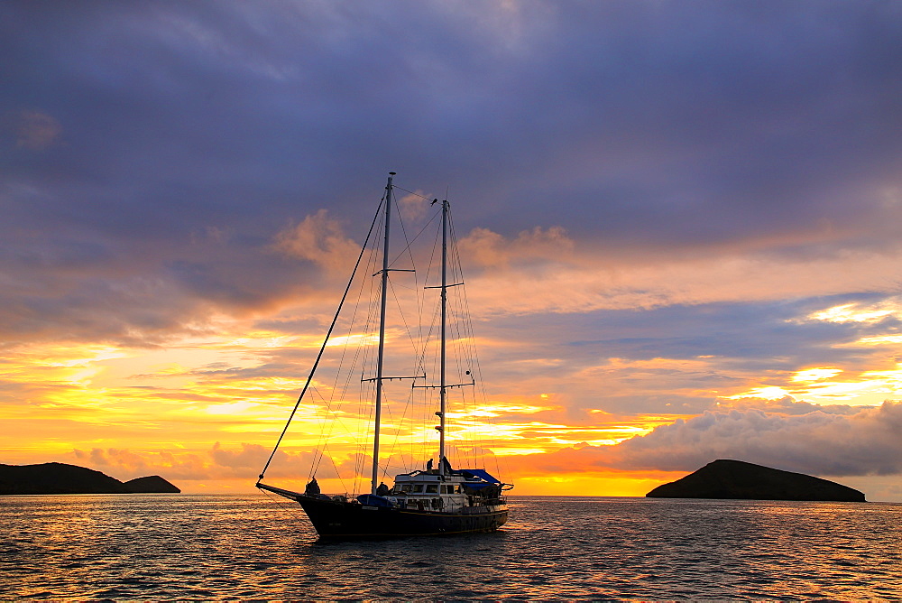 Silhouetted tourist sailboat at sunrise anchored near Chinese Hat island in Galapagos National Park, Ecuador, South America