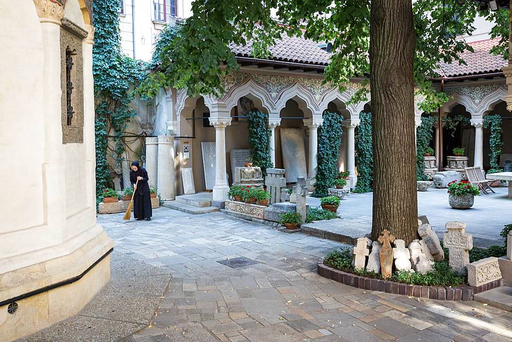 A nun sweeps the grounds of the Stavropoleos Monastery Church (Biserica Manastirea Stavropoleos) early in the morning, Bucharest, Romania, Europe