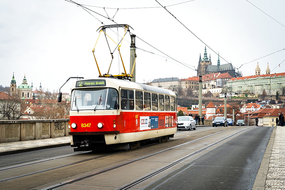 A traditional red tram crosses Manesuv most (bridge) with St. Vitus Cathedral and Prague Castle in the background, Prague, Czech Republic, Europe