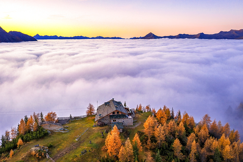 Fog covers the Valmalenco (Val Malenco) with the mountain range of Disgrazia illuminated by sunrise in the background and the Motta mountain hut in the foreground, Valtellina, Lombardy, Italy, Europe