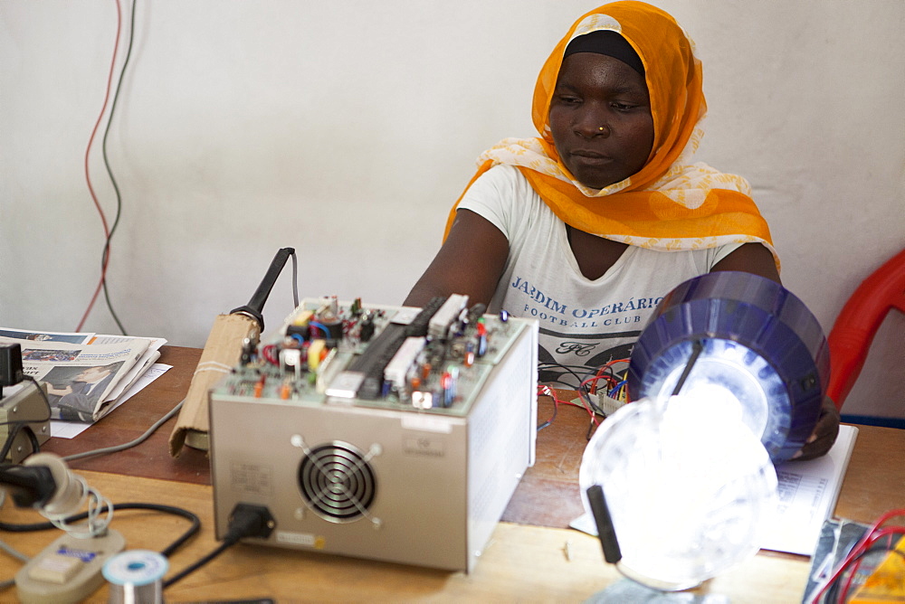 A female solar engineer, known as a solar mama, using a soldering iron to fix the printed circuit board of a solar lamp, Tanzania, East Africa, Africa