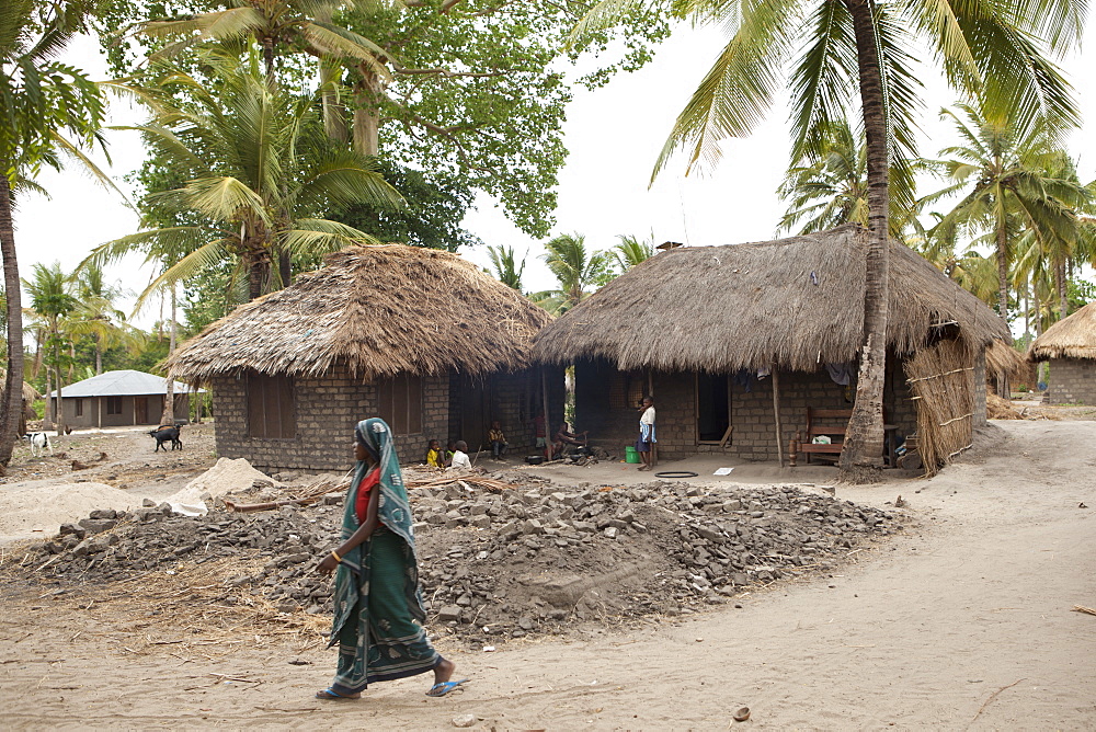 A woman walks past a traditional mud hut home with a solar panel on the top of it, Tanzania, East Africa, Africa