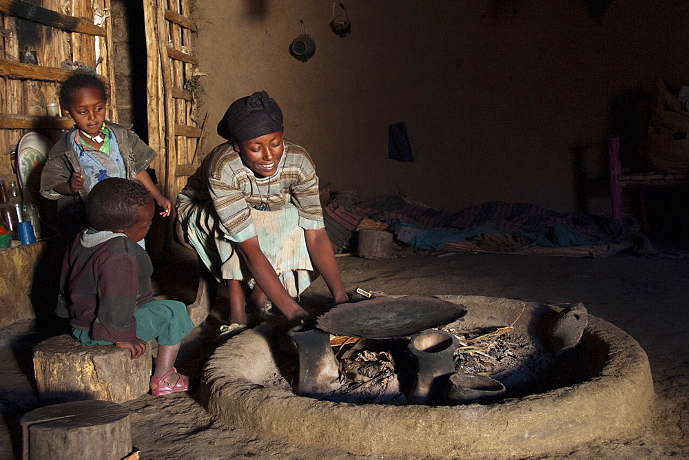 A woman lighting a fire in her home so she can cook dinner, Ethiopia, Africa