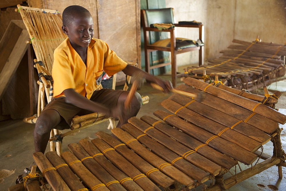 A school boy playing music on a large wooden xylophone at his primary school in Ghana, Africa