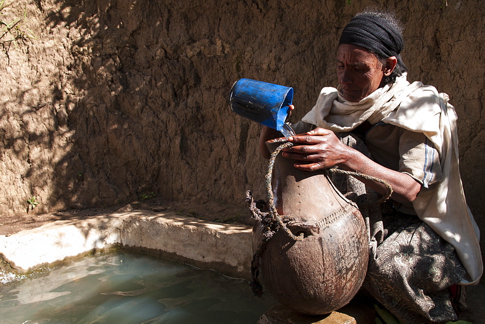 A woman fills a traditional water pot from a capped spring, Ethiopia, Africa