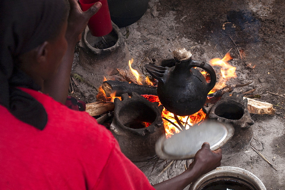 A woman fans the open fire as she makes coffee in a traditional Ethiopian coffee pot, Ethiopia, Africa