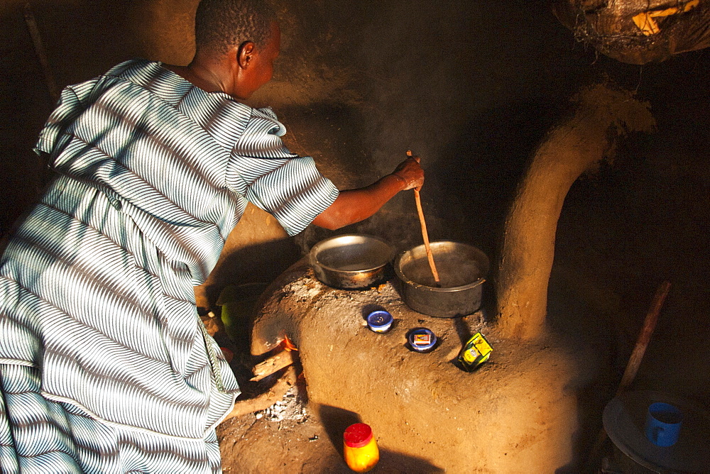 A woman cooking on a fuel efficient stove inside a traditional mud hut kitchen, Uganda, Africa