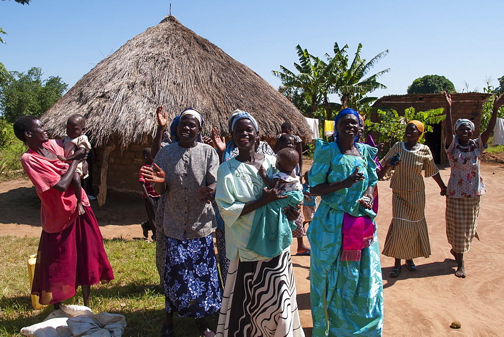 A group of women singing and dancing outside a traditional mud hut with a thatched roof, Uganda, Africa