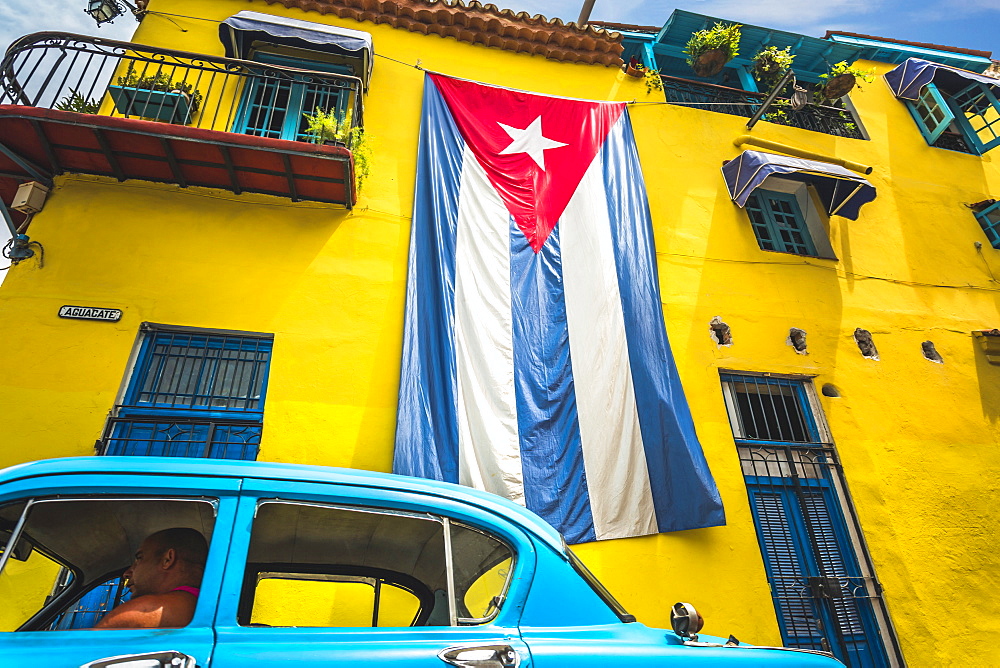 Old American classic car and huge Cuban flag on yellow building in Havana, La Habana (Havana), Cuba, West Indies, Caribbean, Central America