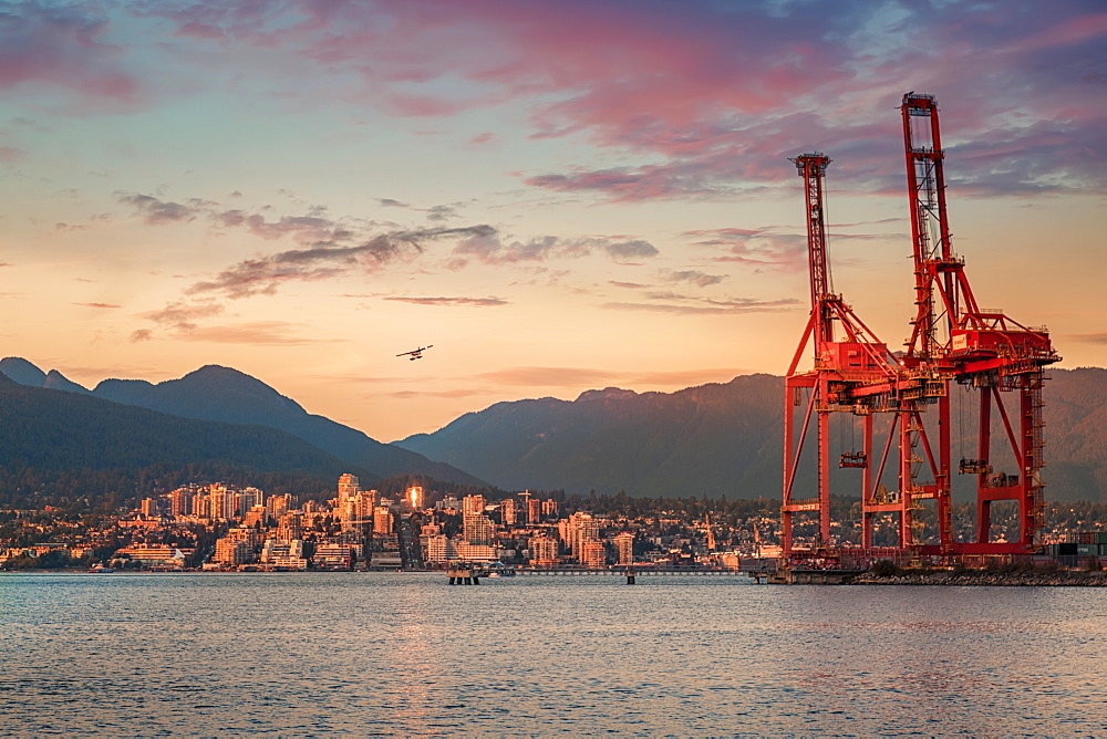 Seaplane flying over North Vancouver at golden hour, Vancouver harbour cranes on the right, Vancouver, British Columbia, Canada, North America