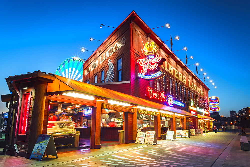 Neon lights illuminating street at night next to Miner's Landing, with the Great Wheel is visible in the background, Seattle, Washington State, United States of America, North America