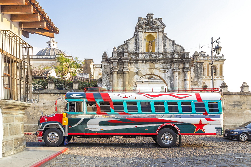 A typical colorful painted chicken bus passing at the entrance gate of San Francisco Church in Antigua, UNESCO World Heritage Site, Guatemala, Central America