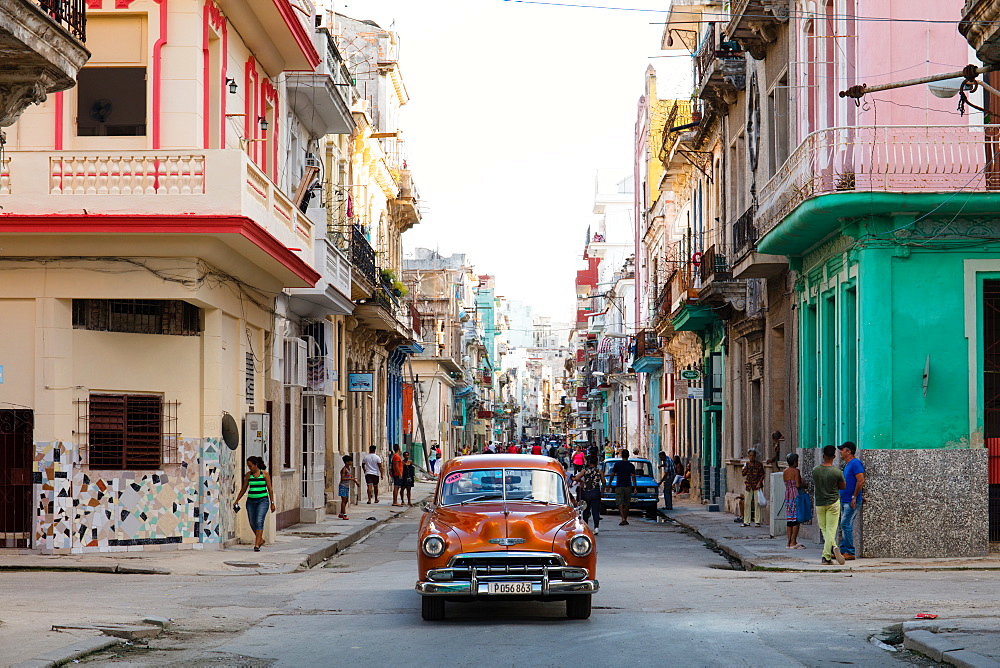 Red vintage car drives along old colourful street in Havana, Cuba, West Indies, Caribbean, Central America