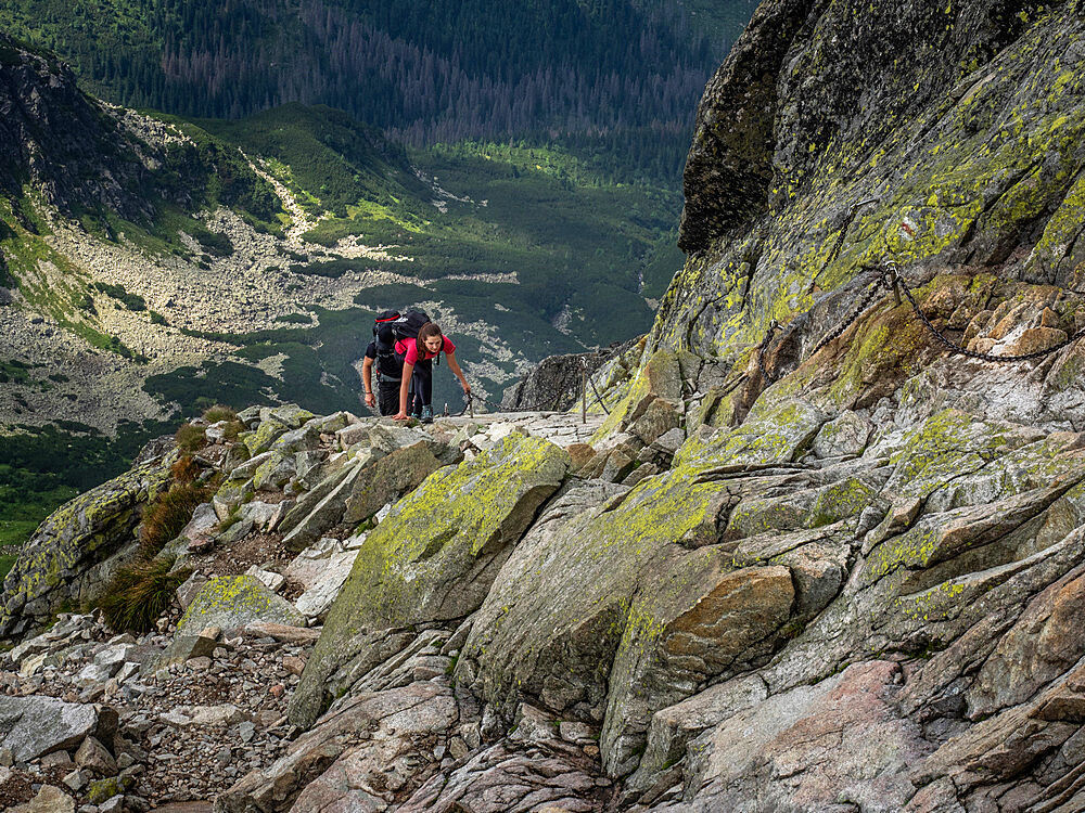 Lady scrambling on Swinica, 2301m, using metal chains, on the Polish and Slovak border in the Tatra Mountains, Poland, Europe