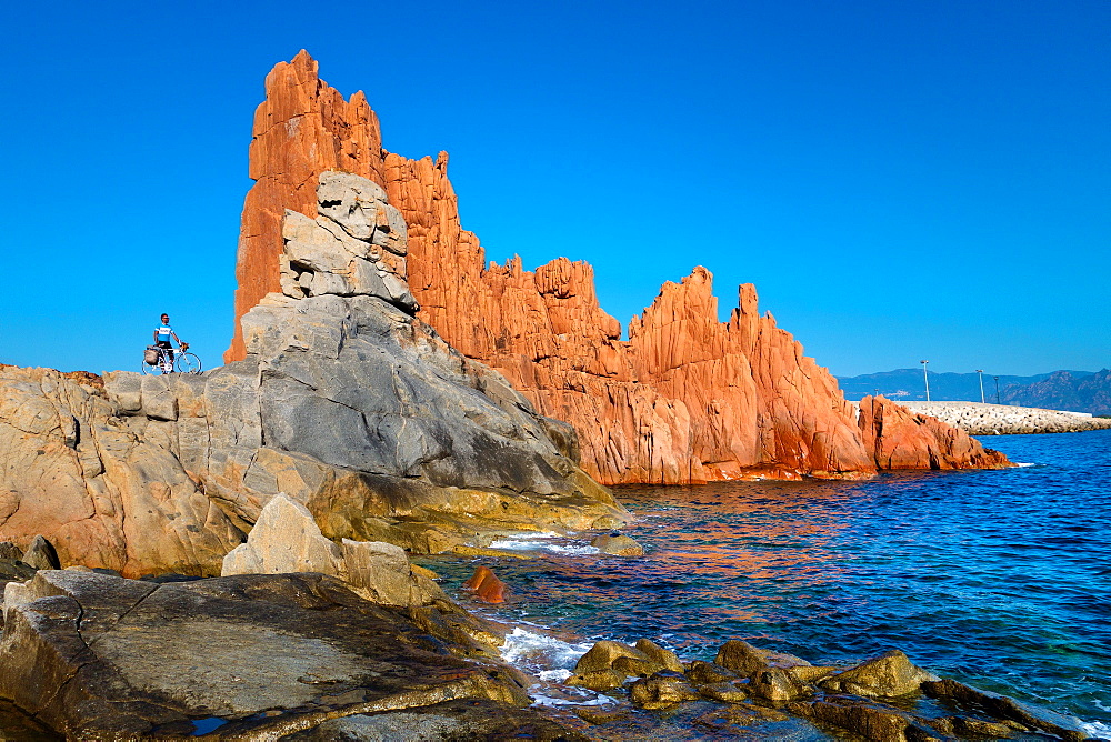 Man with bicycle on rocks by sea in Arbatax, Sardinia, Italy, Europe