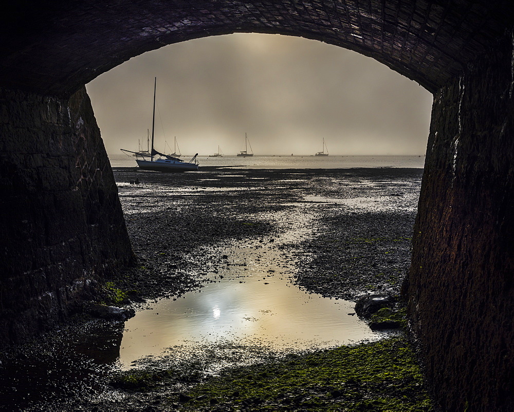 Boats on the Exe estuary in heavy fog viewed through an arch under the Exmouth to Penzance railway line, Starcross, Devon, England, United Kingdom, Europe