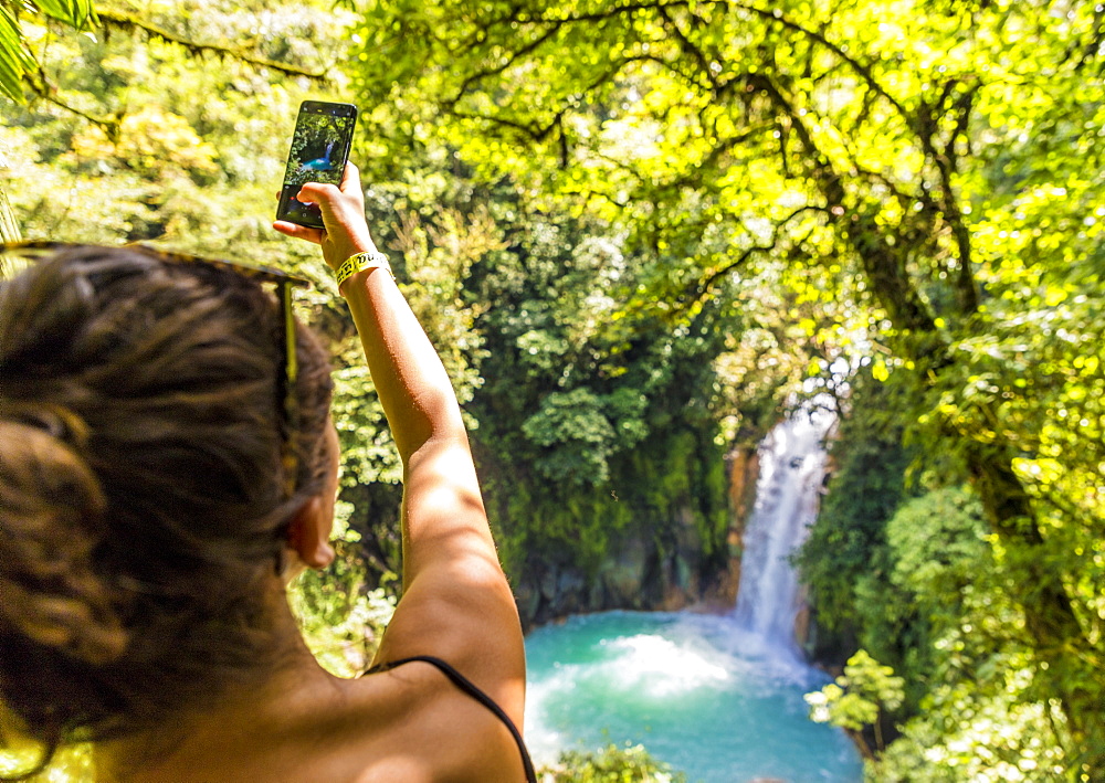 A tourist taking a picture of the Rio Celeste waterfall in Tenorio Volcano National Park, Costa Rica, Central America