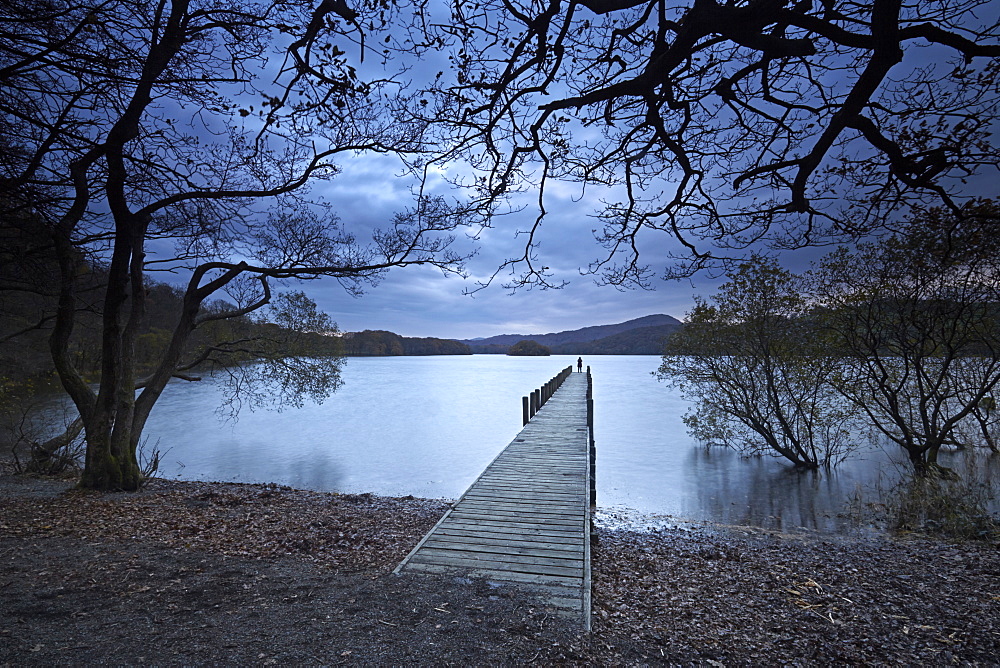 A solitary figure at dusk on Rigg Wood jetty, Coniston Water, Lake District National Park, UNESCO World Heritage Site, Cumbria, England, United Kingdom, Europe