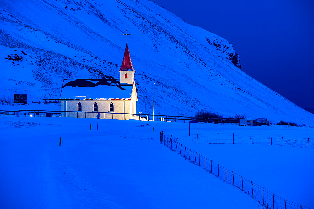 Floodlit church at dawn against snow covered mountains, near Vik, South Iceland, Iceland, Polar Regions