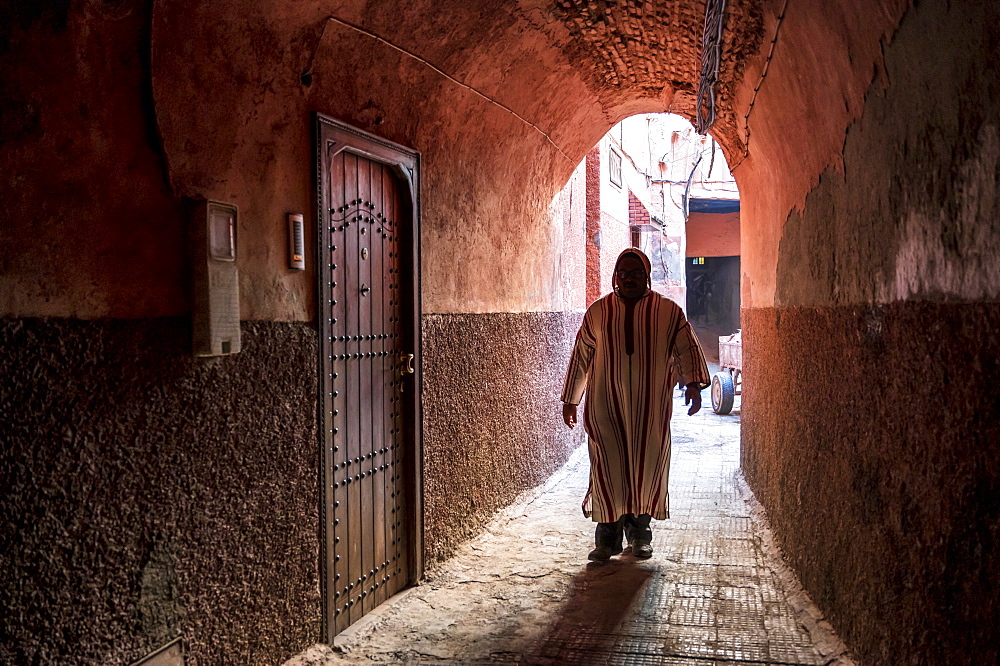 Local man dressed in traditional djellaba walking through archway in a street in the Kasbah, Marrakech, Morocco, North Africa, Africa