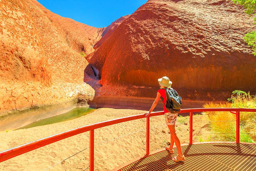 Tourist woman with wide hat standing at balcony admiring Mutitjulu Waterhole at the end of short Kuniya walk in Uluru-Kata Tjuta National Park, UNESCO World Heritage Site, Northern Territory, Australia, Pacific