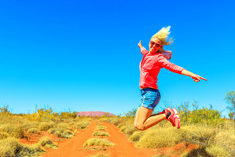 Happy tourist woman jumping at Uluru (Ayers Rock) in Uluru-Kata Tjuta National Park, Northern Territory, Central Australia, Pacific