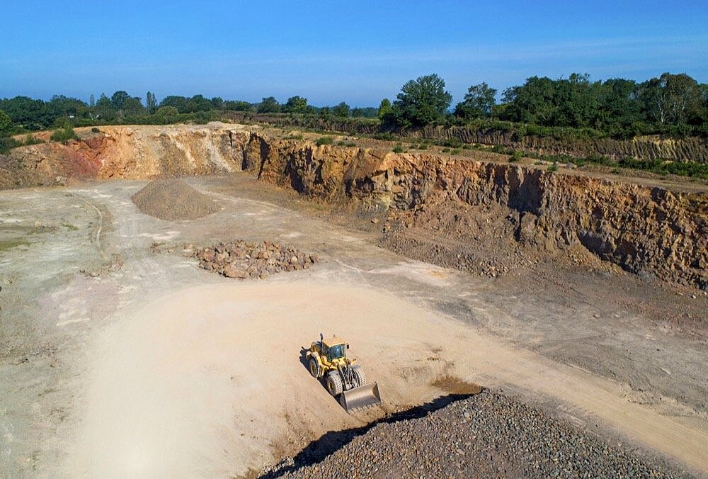 Aerial view of a digger in a quarry in front of a pile of rubble.