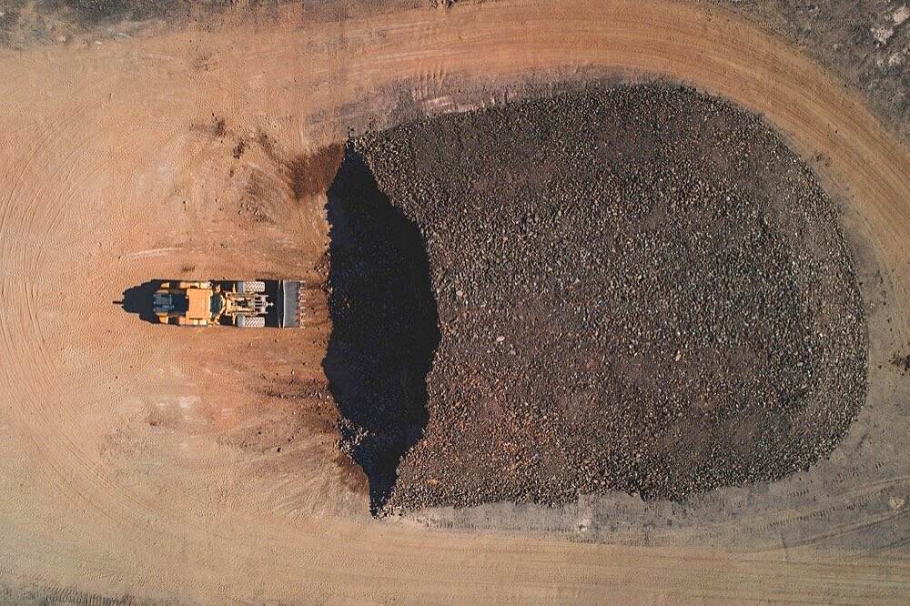 Aerial view of a digger in a quarry in front of a pile of rubble.